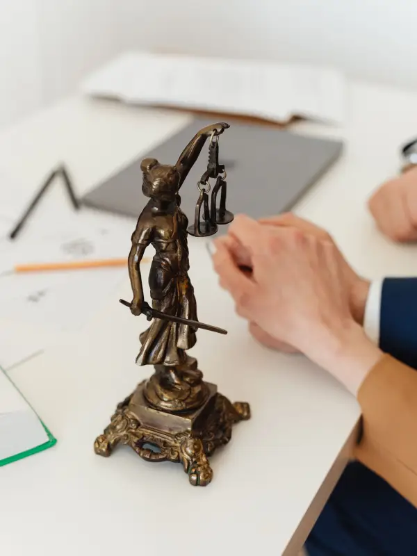 A Lady Justice figurine on a consultation desk, a lawyer's and a client's hands in the background