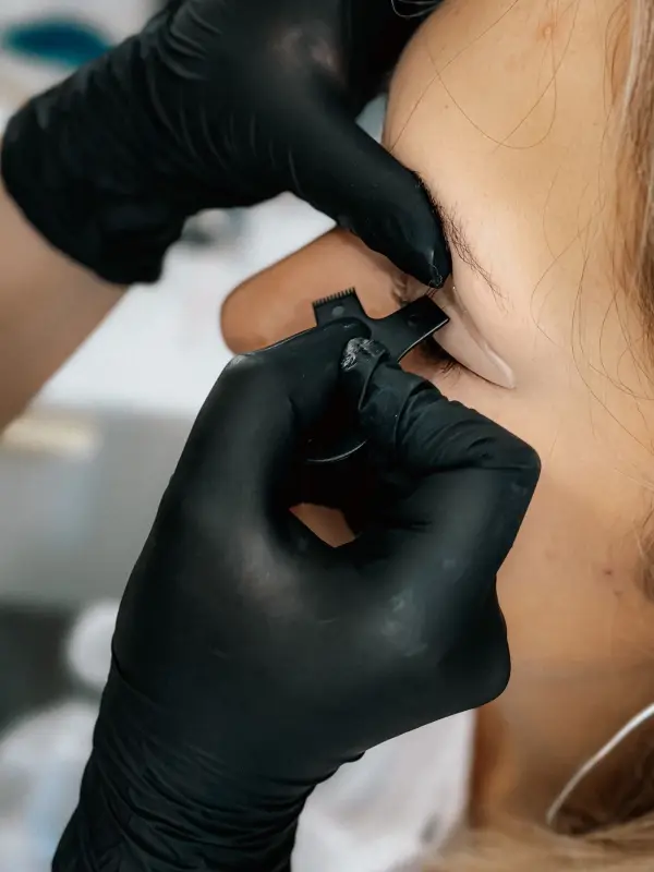 A specialist in black gloves works on a client’s brow, face mostly out of frame